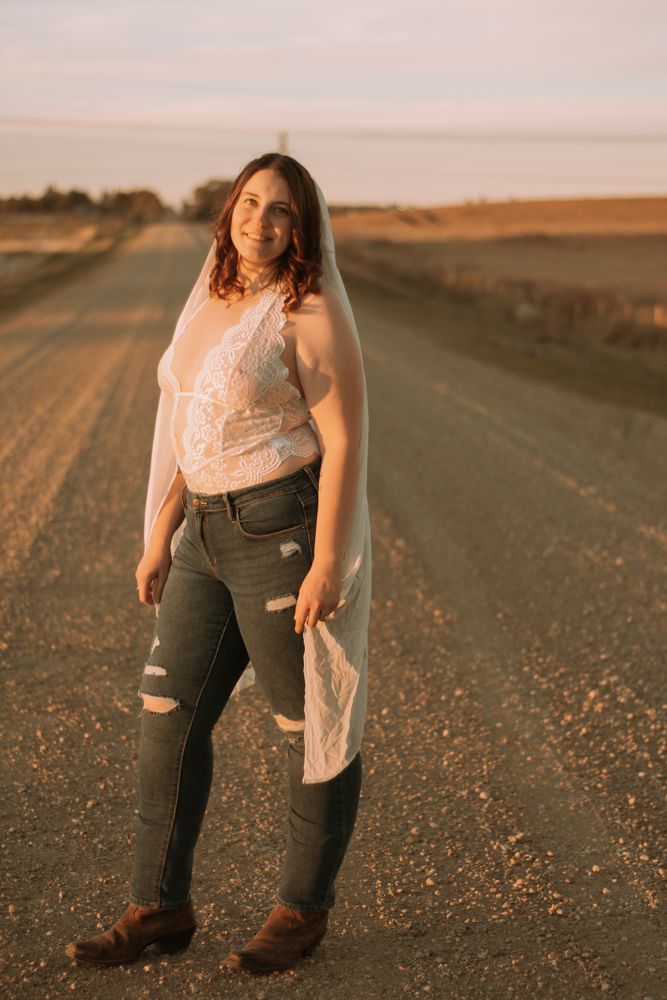 Portrait along a rural road with lace top and ripped jeans in warm evening light.