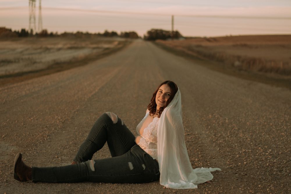 Artistic shot of person sitting on rural road with flowing veil in evening light.