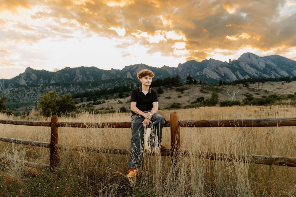 Boy poses sitting down on fence for sunset senior photos and portraits in Boulder, Colorado outside and in nature photos