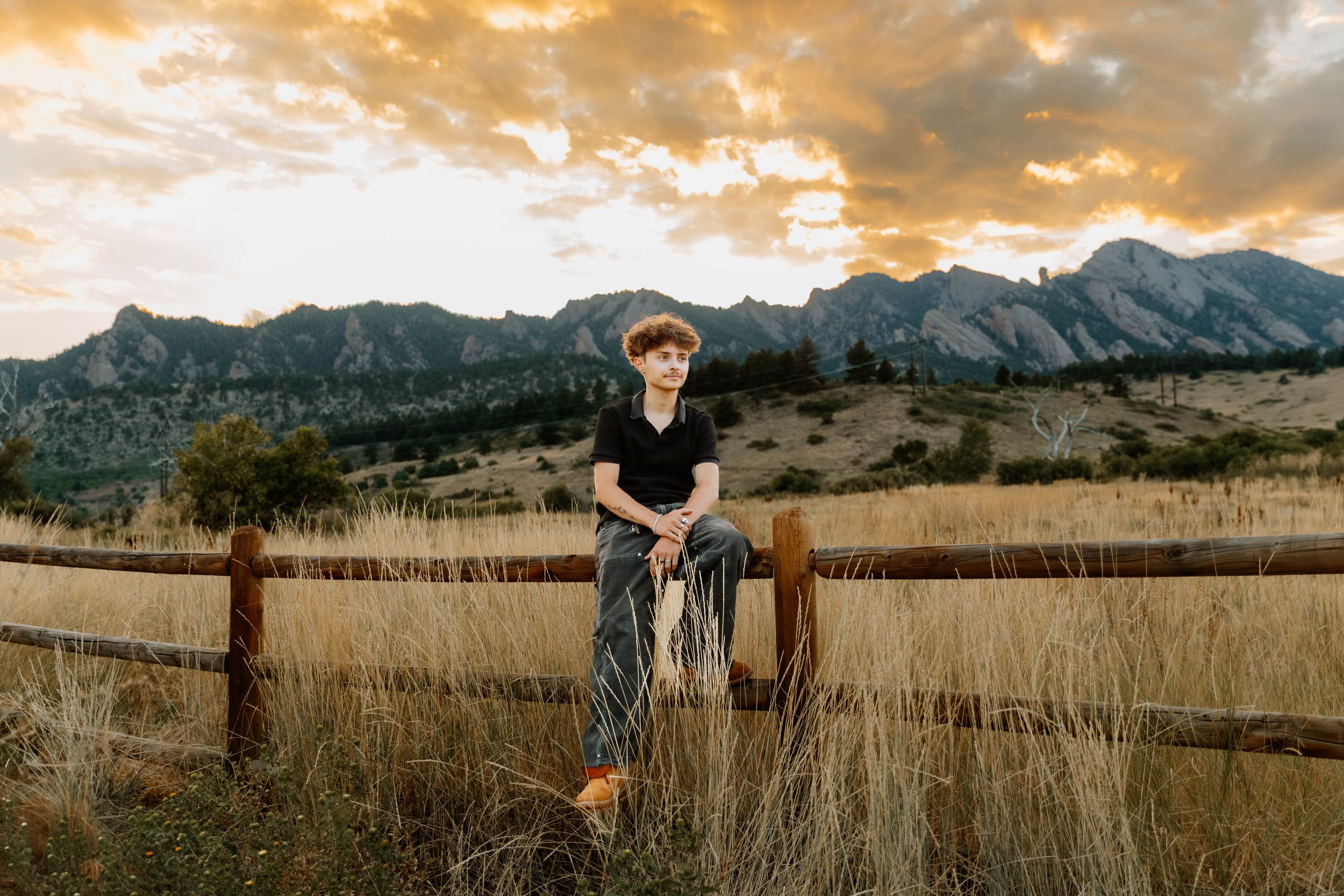 Boy poses sitting down on fence for sunset senior photos and portraits in Boulder, Colorado outside and in nature photos