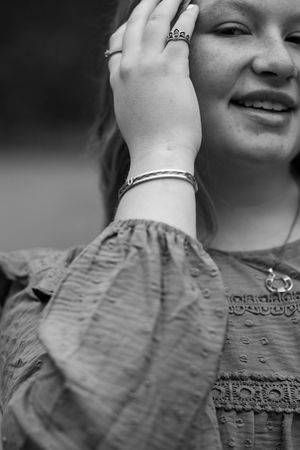 Black and white portrait of a smiling young woman wearing a bracelet and ring, touching her face gently.