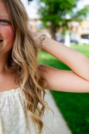Young girl with long wavy blonde hair wearing a silver chain bracelet and white tank top with her Marion senior photographer.
