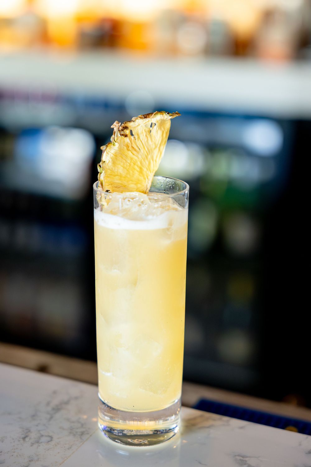 Tall pineapple cocktail garnished with a fresh pineapple wedge on a marble bar.