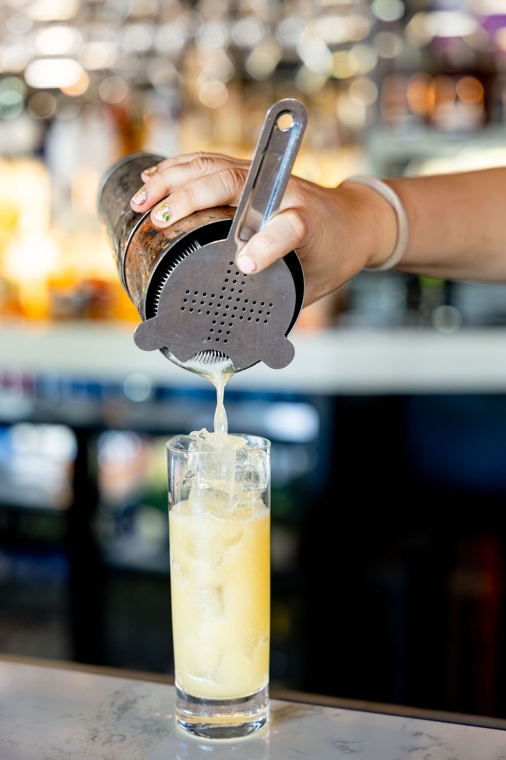 Bartender pouring a creamy cocktail from a shaker into a tall glass with ice.