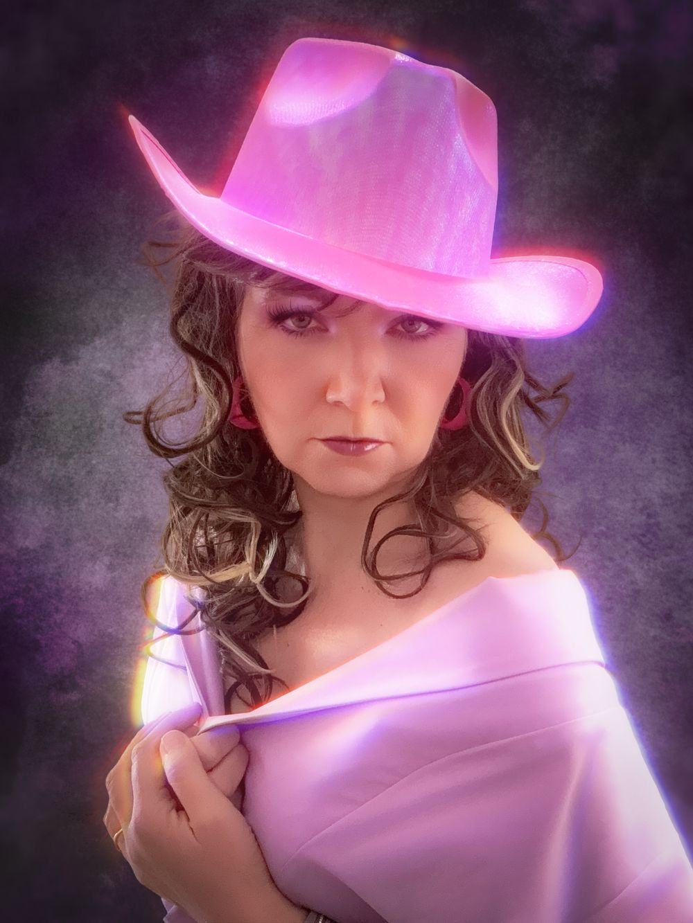 Awkward 80s glamour portrait of a woman wearing pink chiffon off the shoulders with pink cowboy hat, soft focus, glow and intense stare.