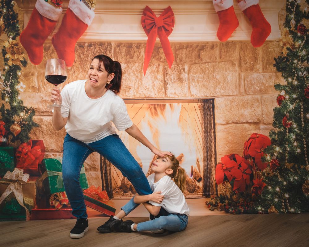 Awkward christmas family photo of mum holding a large glass of wine while daughter pulls on her leg, in front of a Christmas fireplace