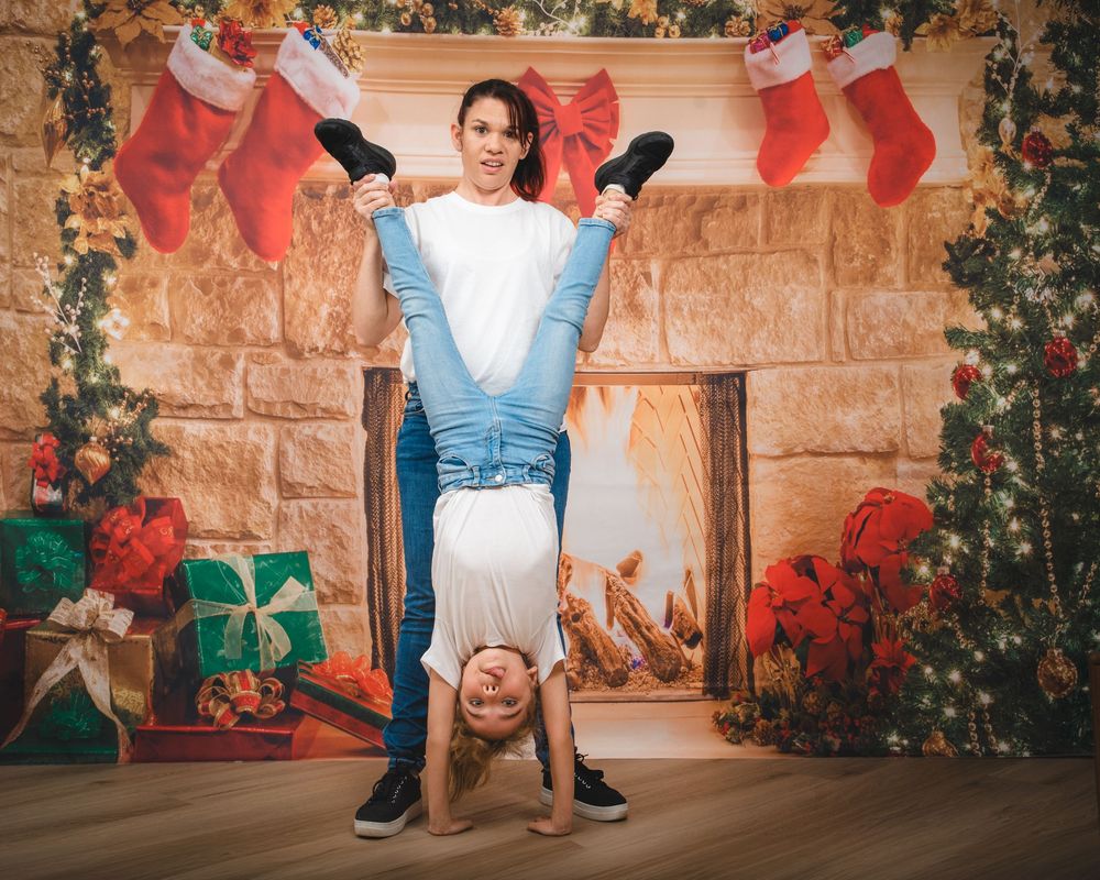 Awkward family photo of mum holding daughter upside down, wearing matching clothes, in front of a christmas fireplace scene