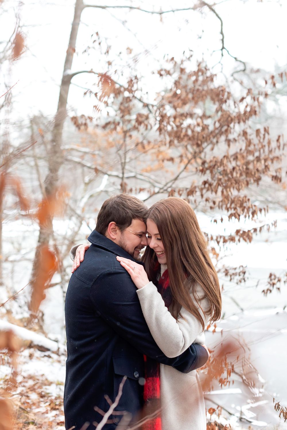 Couple embracing tenderly in snowy winter forest with autumn leaves.