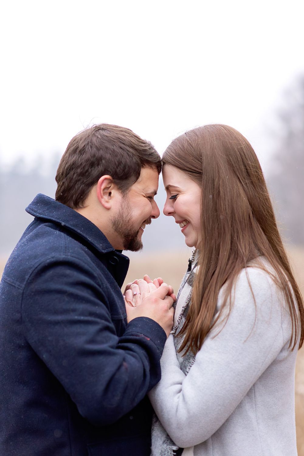 Close-up of smiling couple touching foreheads and holding hands together on a cold winter day.