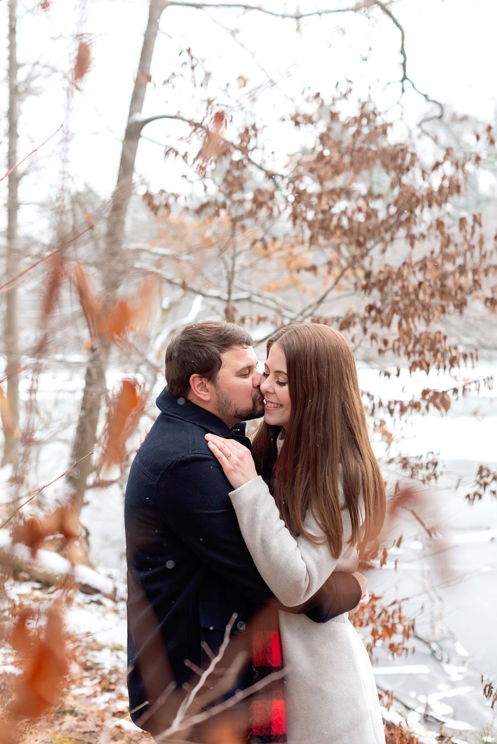 Romantic couple embracing and kissing among snow-covered trees in winter forest.