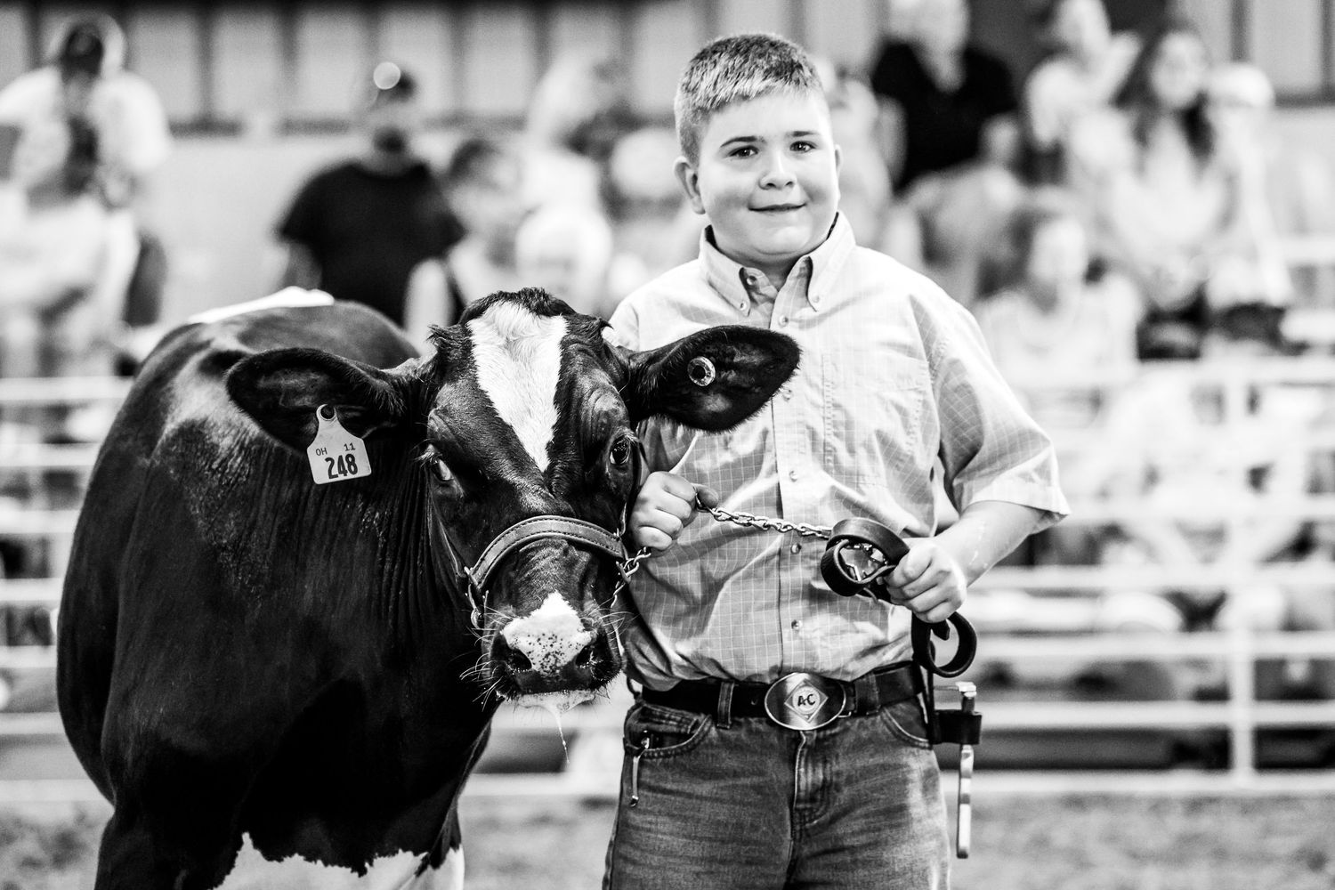 Young boy proudly showing his black and white cow at a livestock competition in a black and white photo.