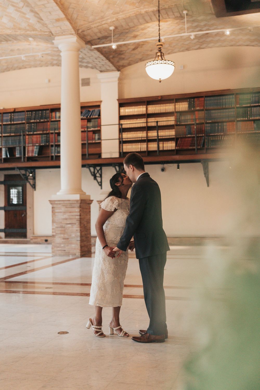 Couple sharing a kiss in an elegant library venue with bookshelves and columns on their wedding day.