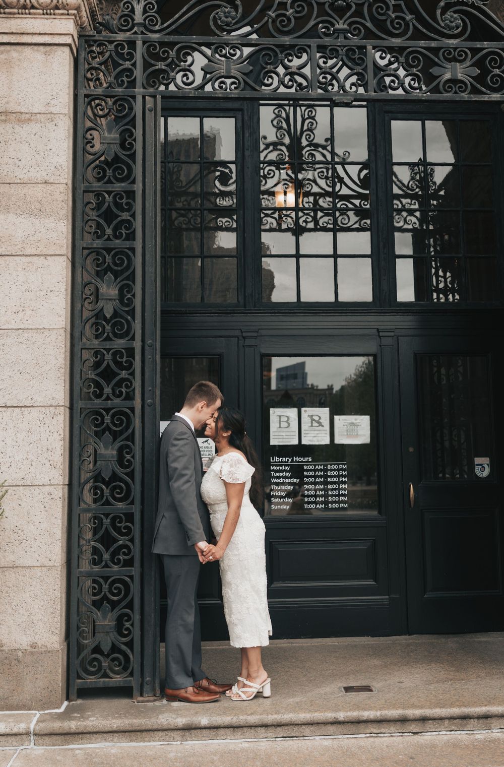 Couple sharing a romantic kiss in front of an ornate black iron door of a historic library building.