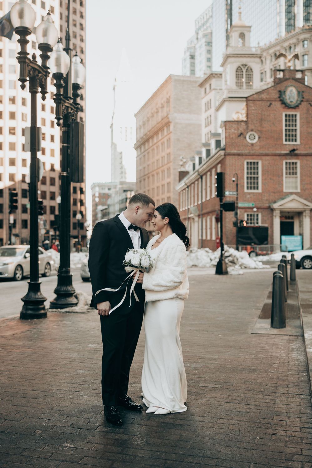 Bride and groom share a romantic moment on a brick street in Boston, with historic buildings in the background.
