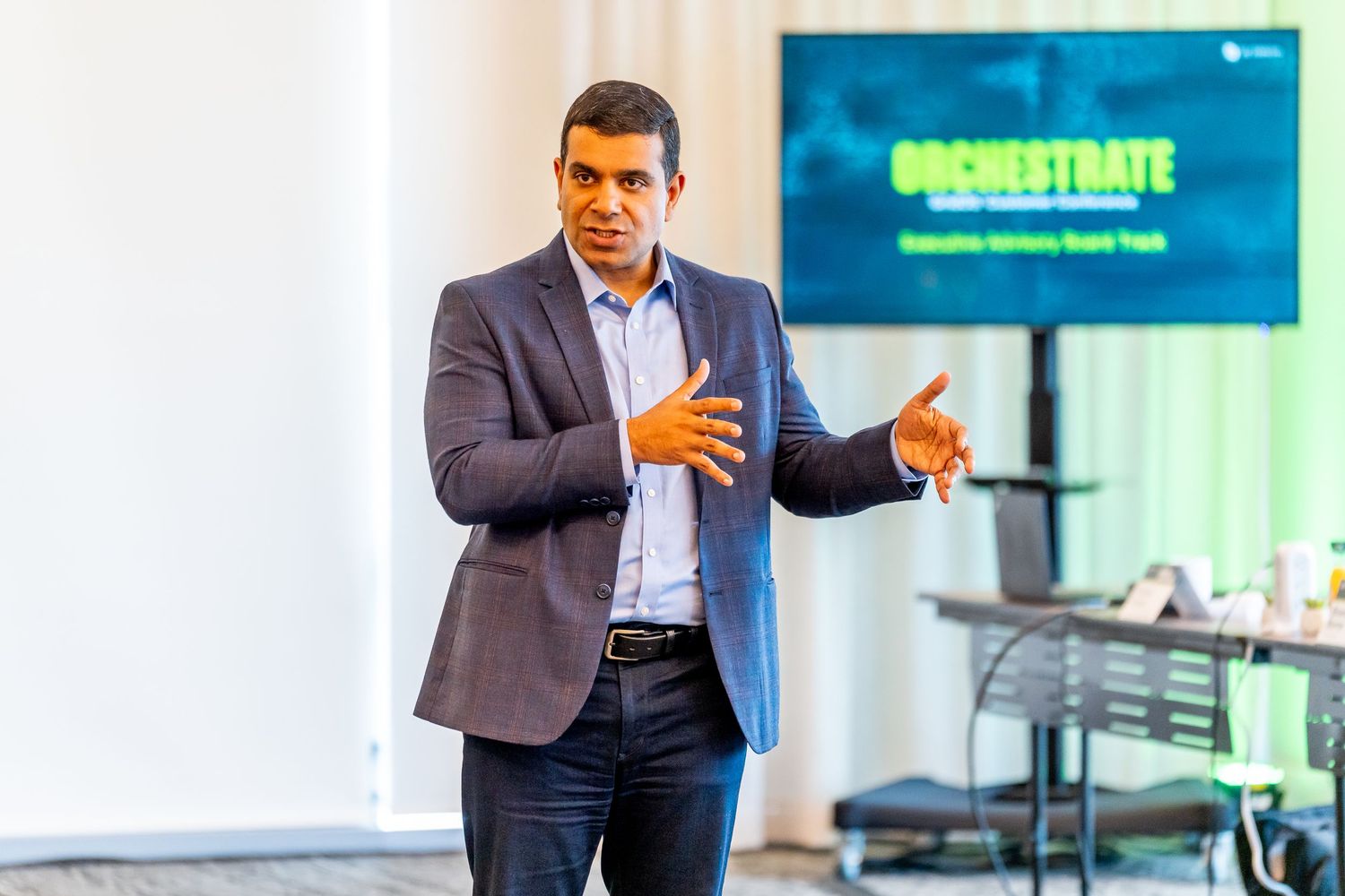 Business speaker presenting at Orchestrate Executive Advisory Board event, gesturing confidently in blazer.