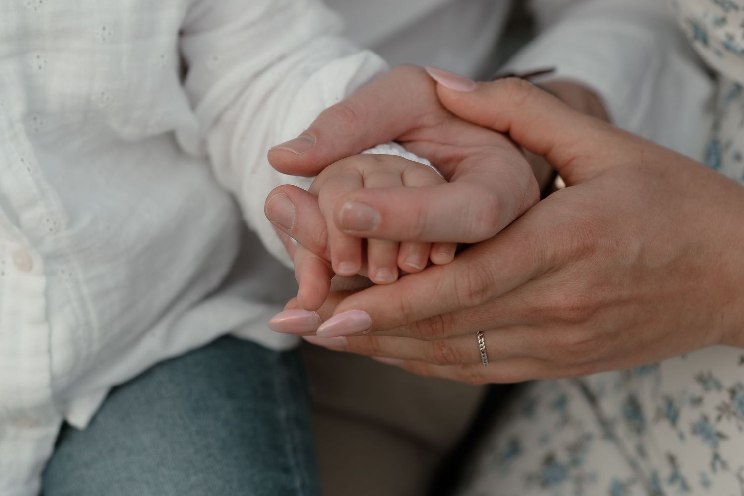 Adult hands gently cradling a newborn baby's tiny feet and toes in a tender, loving close-up moment.