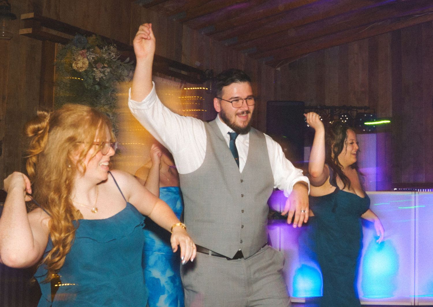 Guests dancing and celebrating joyfully at a rustic indoor wedding reception party.