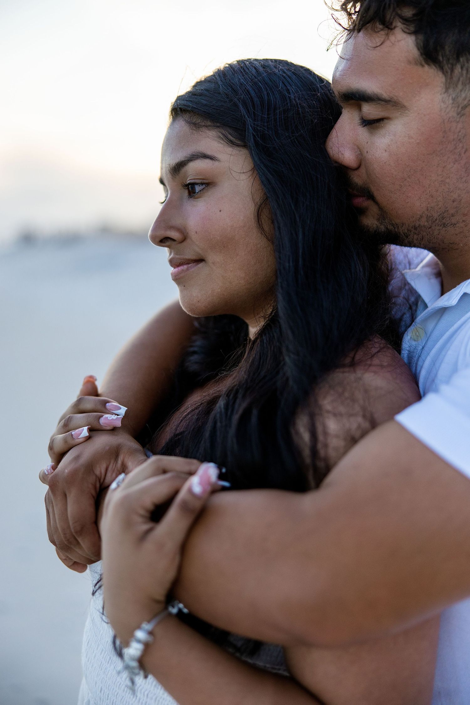 A smiling couple poses together on the beach of pensacola, florida facing each other
