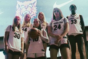 Six female basketball players in Evanston jerseys pose together on a court in front of a large Nike display backdrop.