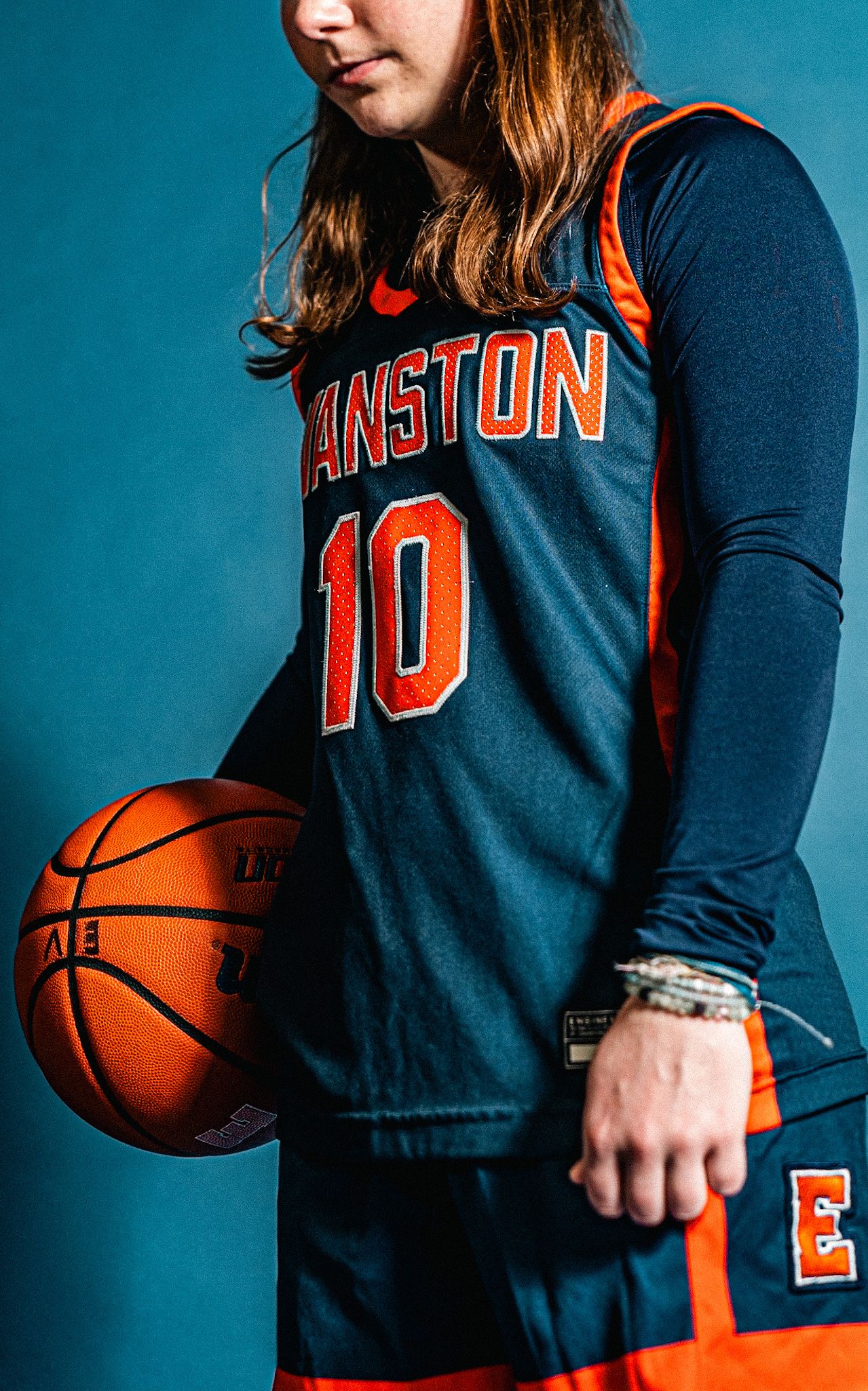 Basketball player wearing navy and orange Evanston #10 jersey holds a Spalding basketball against a blue background.