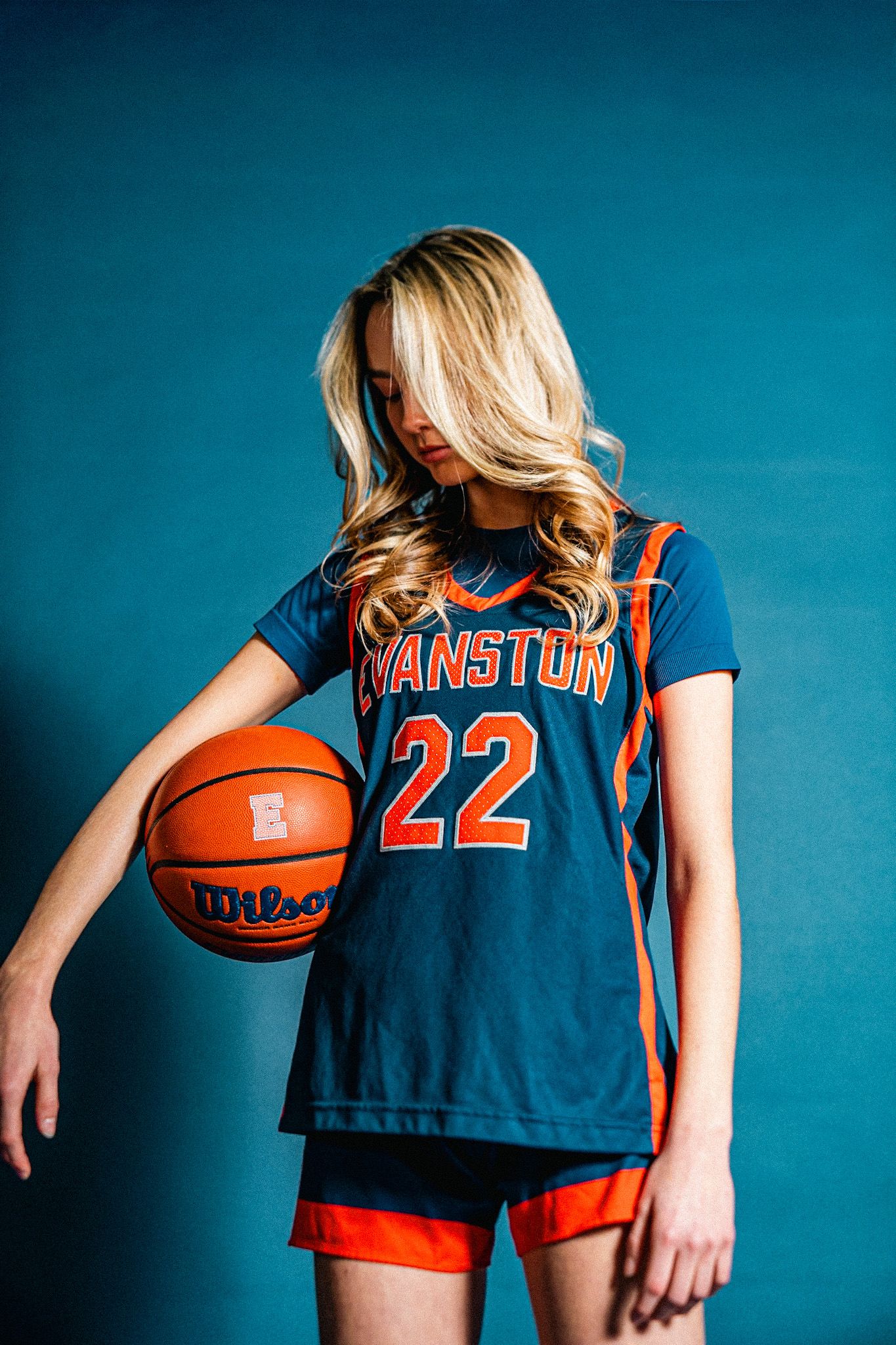 Young female basketball player in Evanston #22 navy and orange jersey holding a Wilson basketball.