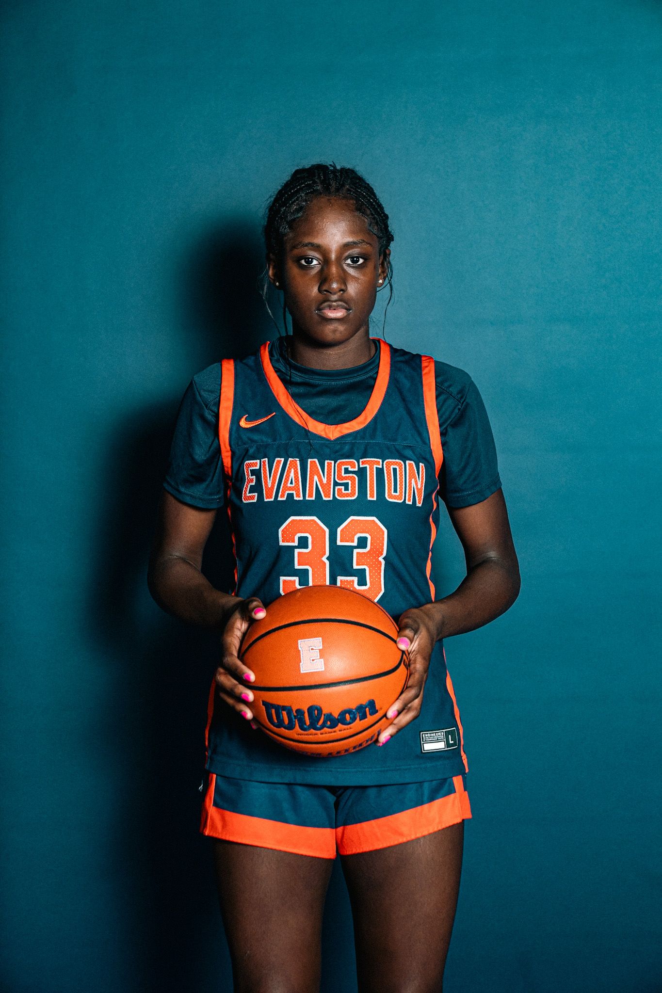 Evanston #33 female basketball player in navy and orange Nike uniform holding a Wilson basketball.