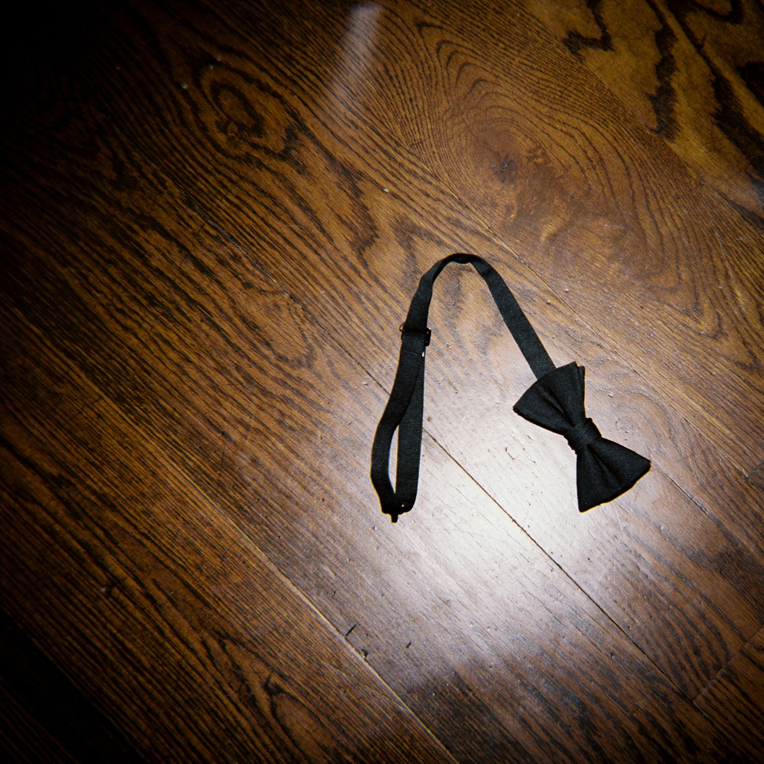 Black bow tie lying on a dark wooden floor at a formal event.