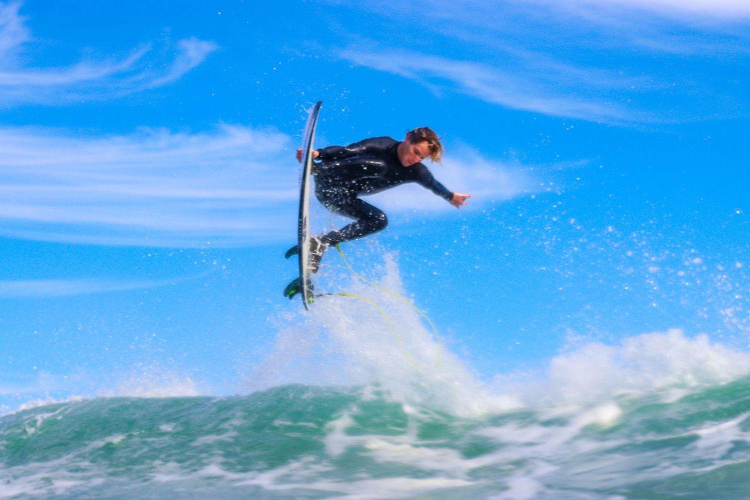 San Diego surf photography of a male surfer in a wetsuit catching big air above a wave.
