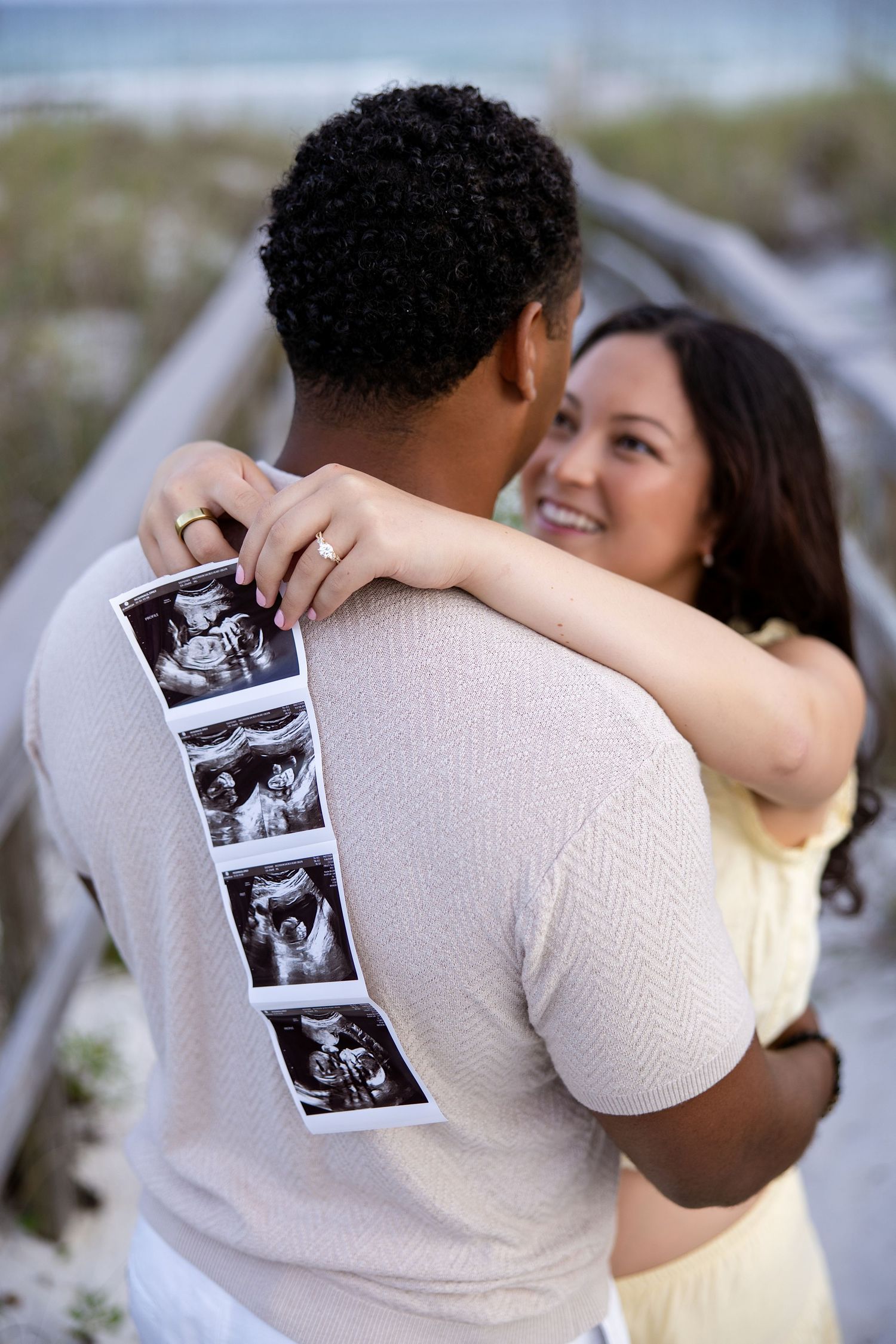 A smiling couple poses together on the beach of pensacola, florida facing each other