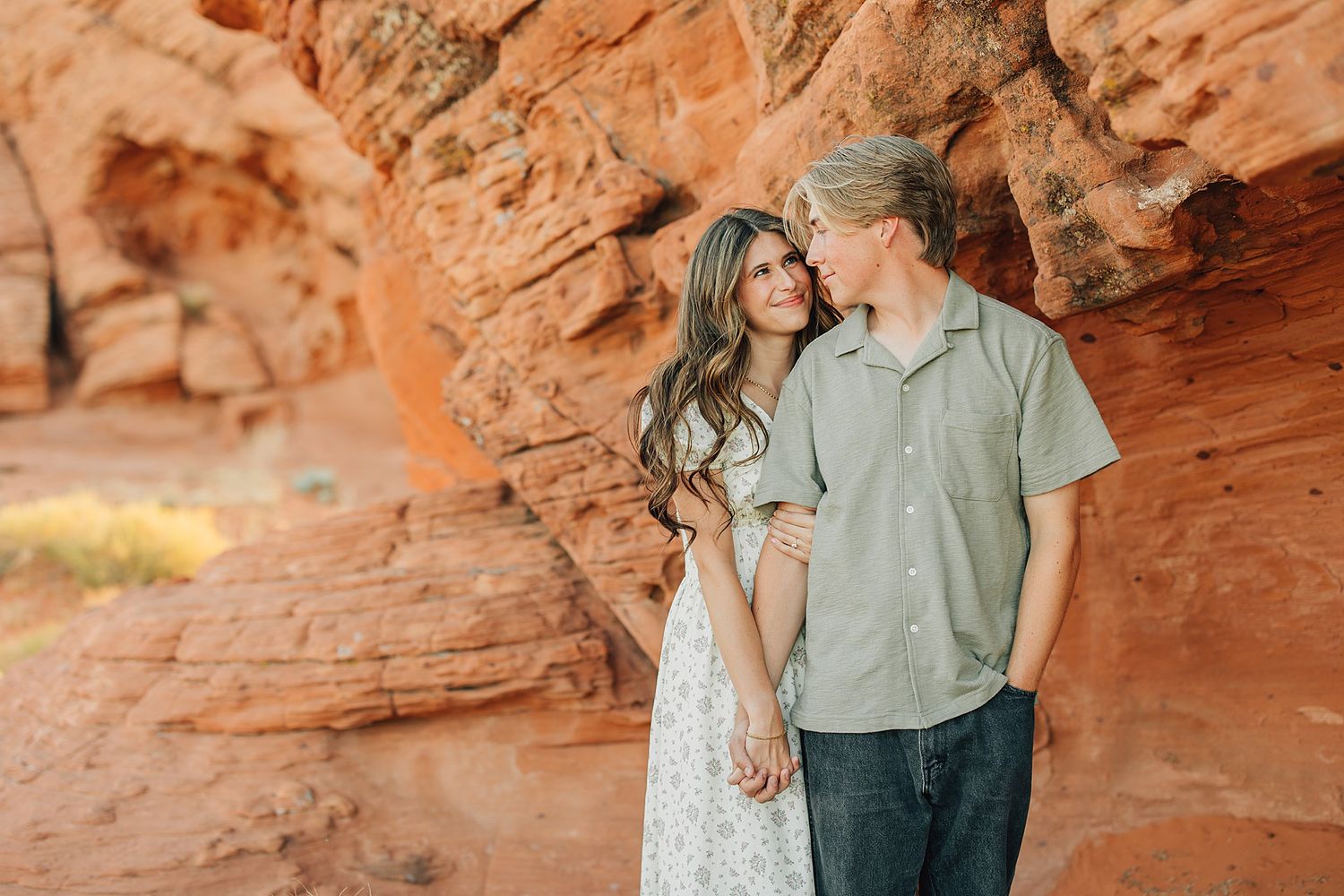 Couple standing together against red rock canyon walls, woman in floral dress, man in sage green shirt.