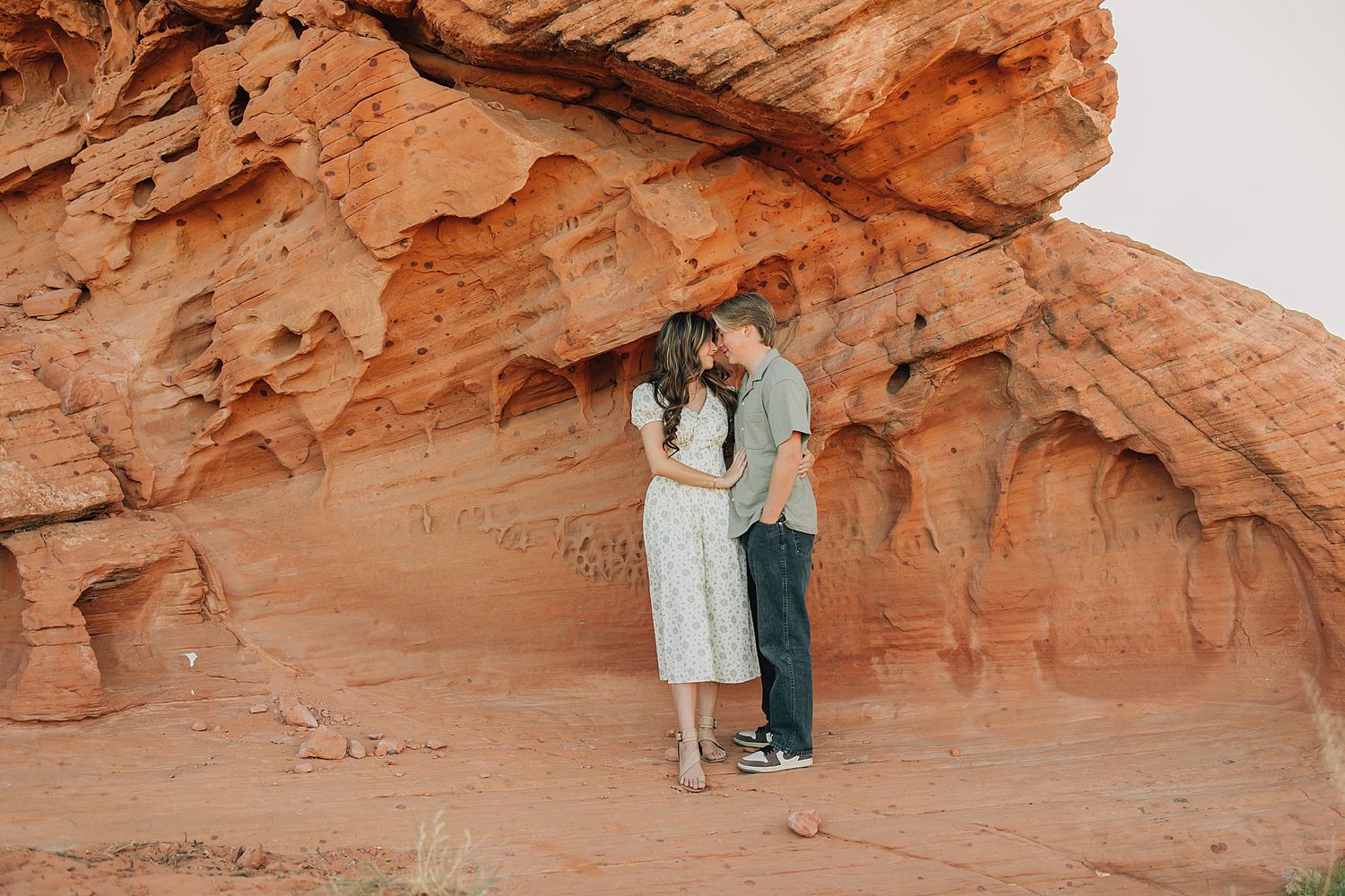 Couple sharing a romantic kiss in front of stunning red rock formations in a desert landscape.