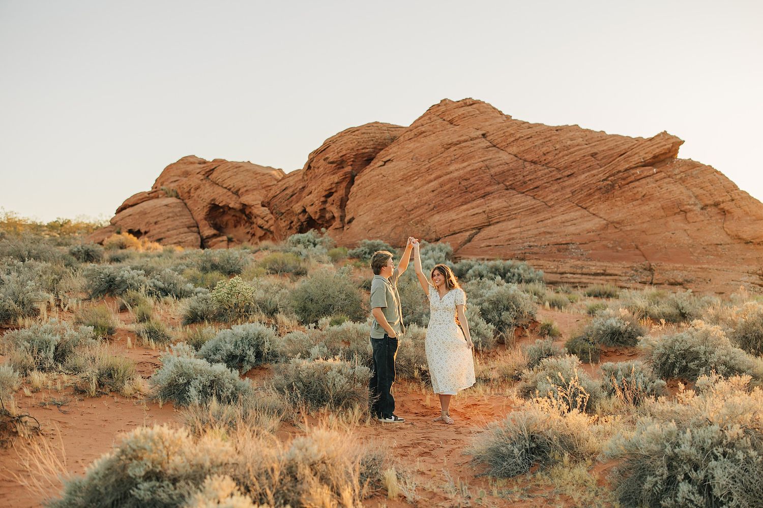 Couple dancing together in a desert landscape with red rock formations and sagebrush at golden hour.