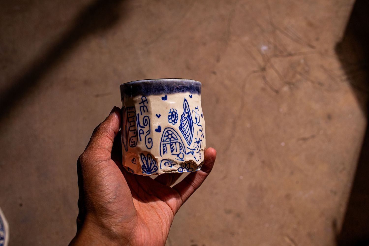 Hand holding a blue and white painted ceramic cup with floral folk art designs on sandy background.