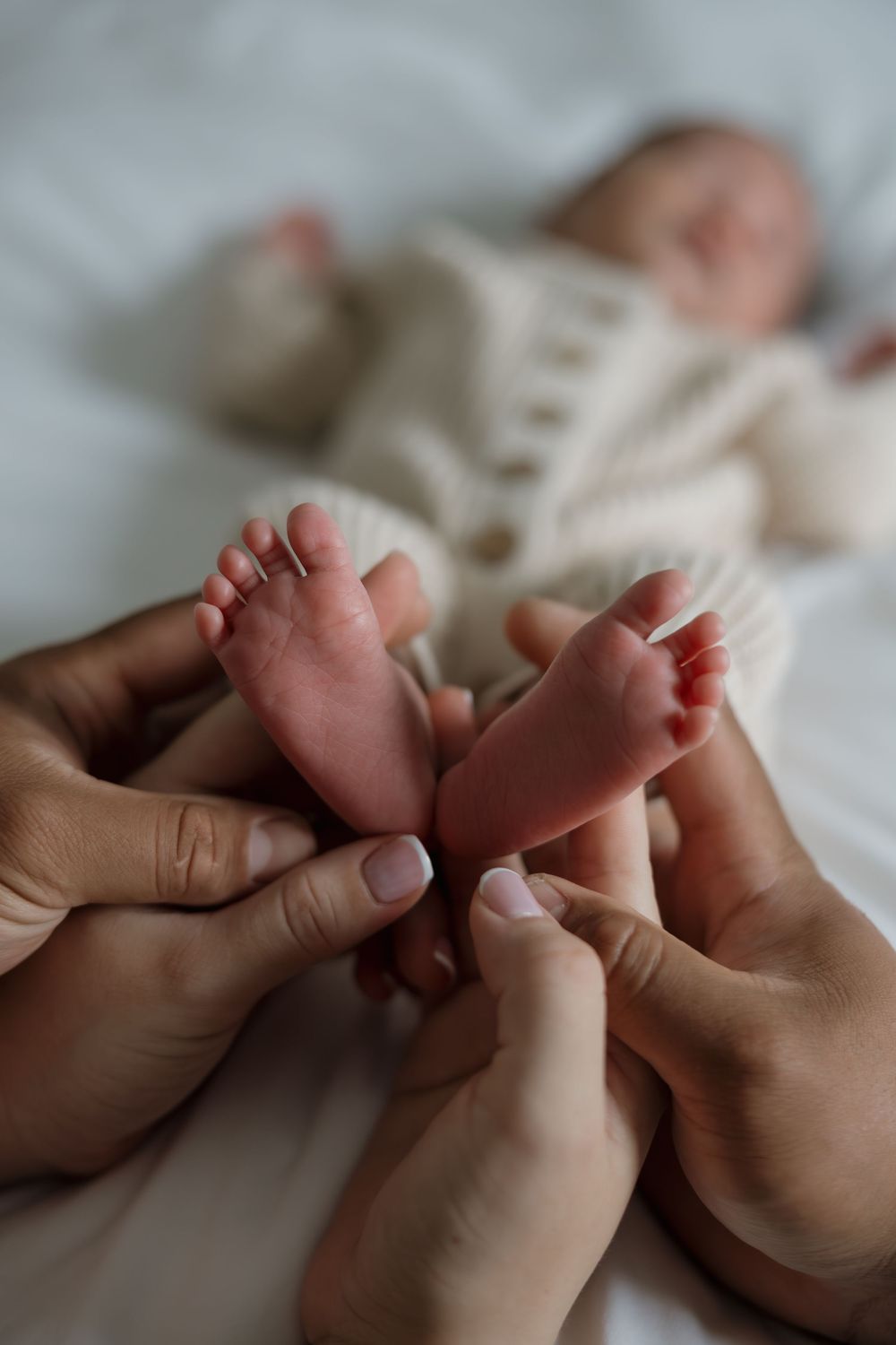 Two parents cradle their newborns tiny feet in their hands while baby rests on a white blanket.
