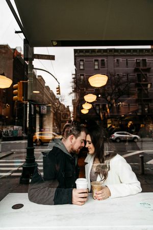 A couple shares coffee and conversation at a cozy cafe window in an urban setting.