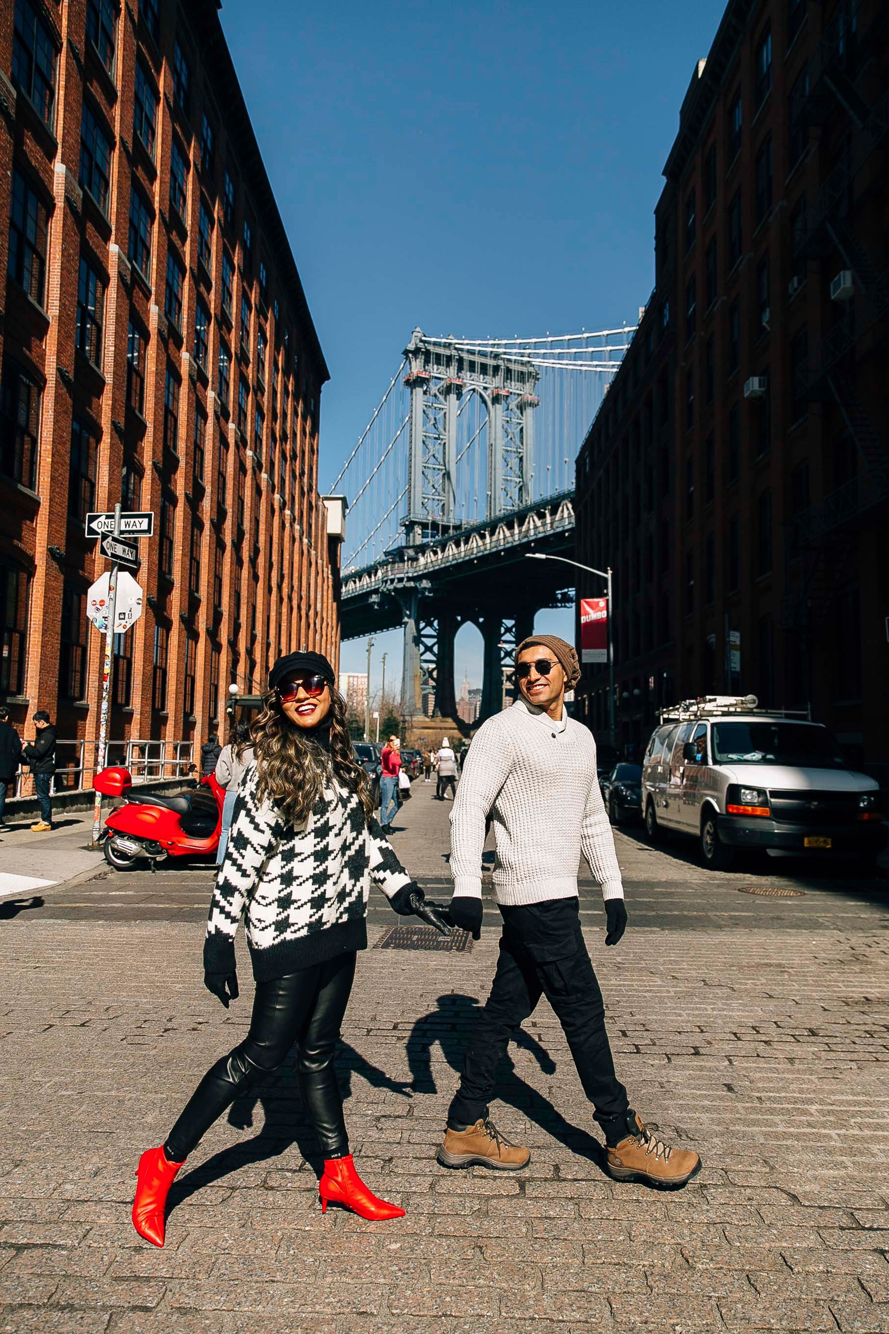 Couple walking on cobblestone street with Manhattan Bridge view in DUMBO Brooklyn.