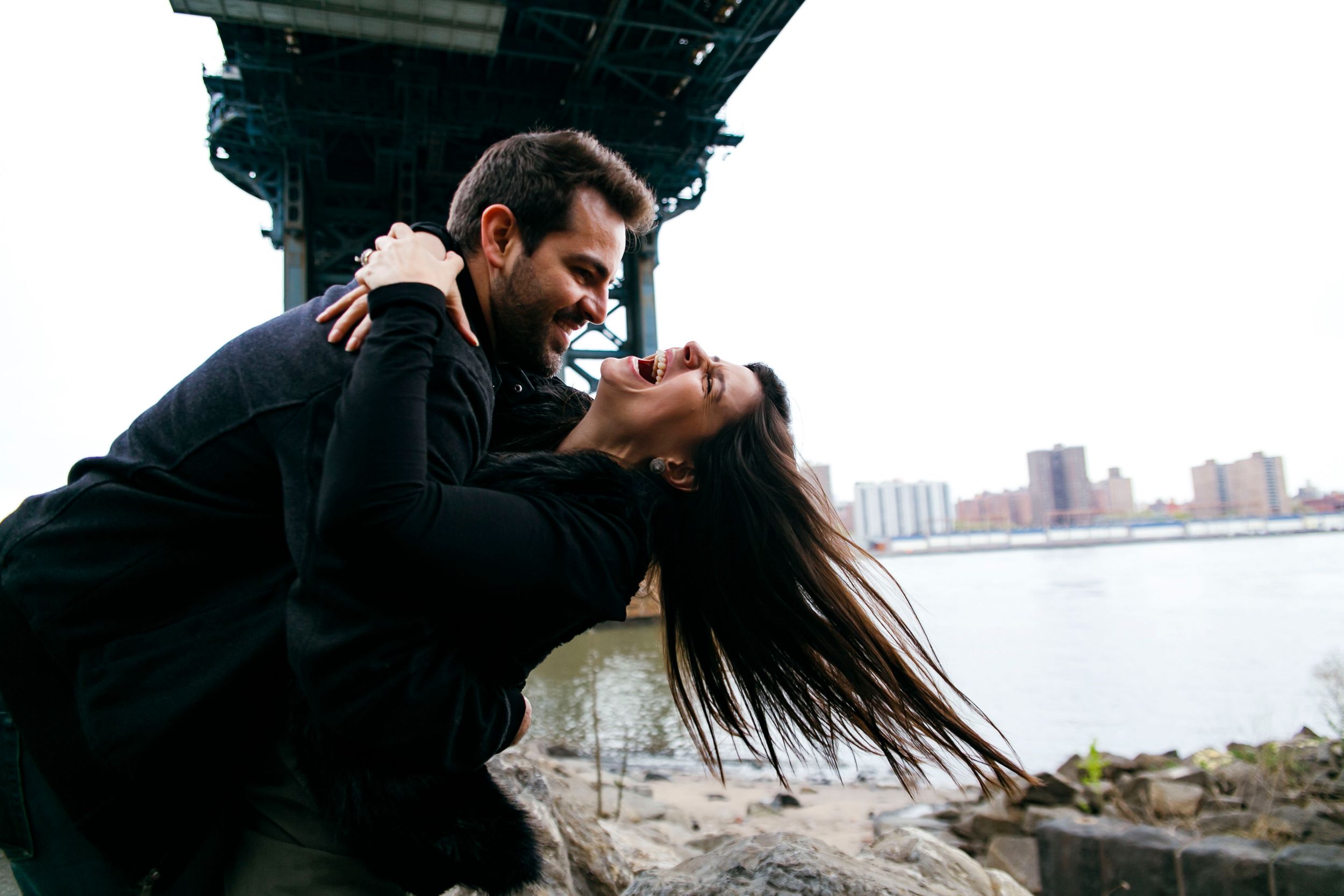 Romantic couple embracing under bridge with waterfront view.