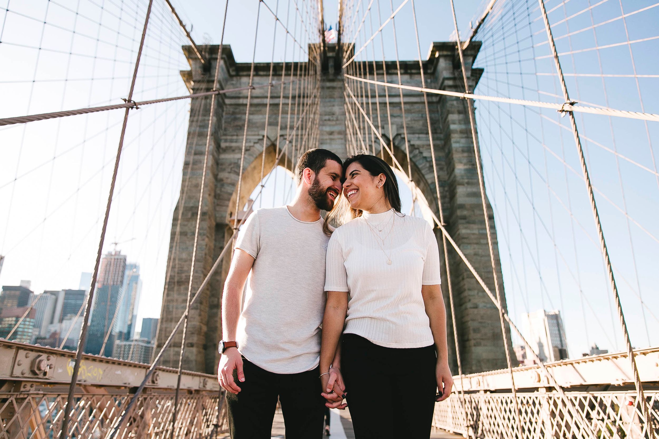 Couple sharing intimate moment on Brooklyn Bridge with Manhattan skyline in background.