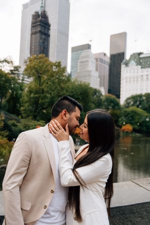 A couple shares an intimate moment in front of Central Park with Manhattan skyscrapers in the background.