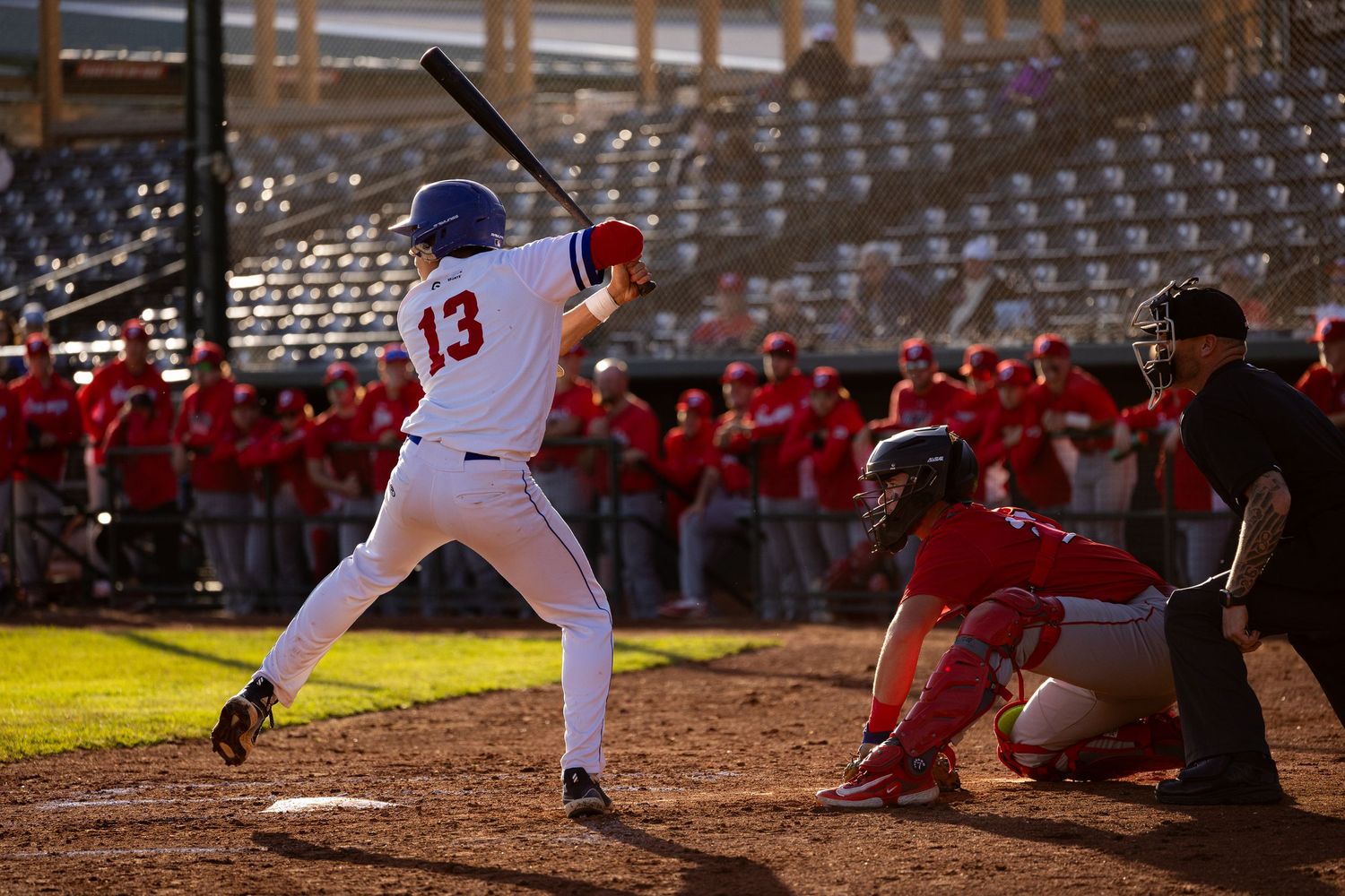 Brooks Bombers (WCBL) batter number 13 stands ready at plate with catcher and umpire at sunset.