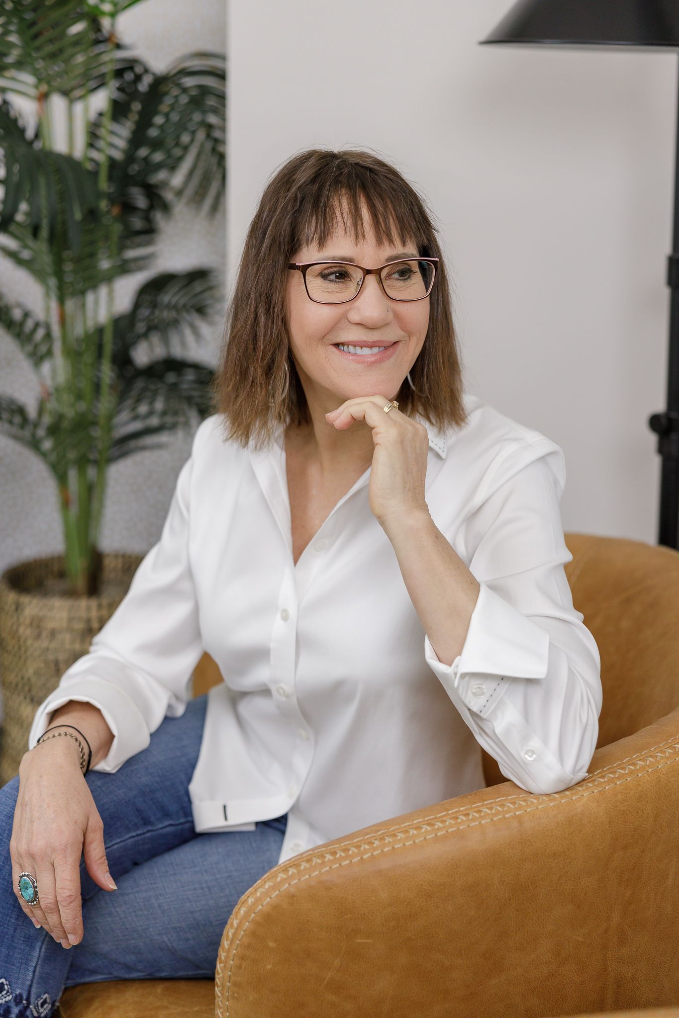 woman sitting in chair wearing glasses, white button down and jeans with hand lightly touching under chin smiling Tacoma, WA headshot