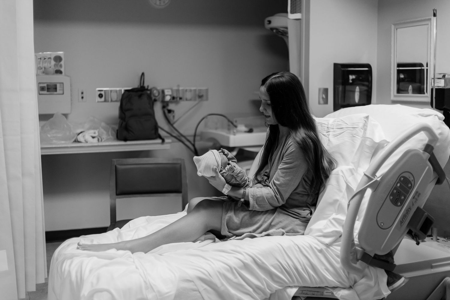 A newborn baby rests in a hospital bassinet, wearing a diaper with a yellow umbilical cord clamp.