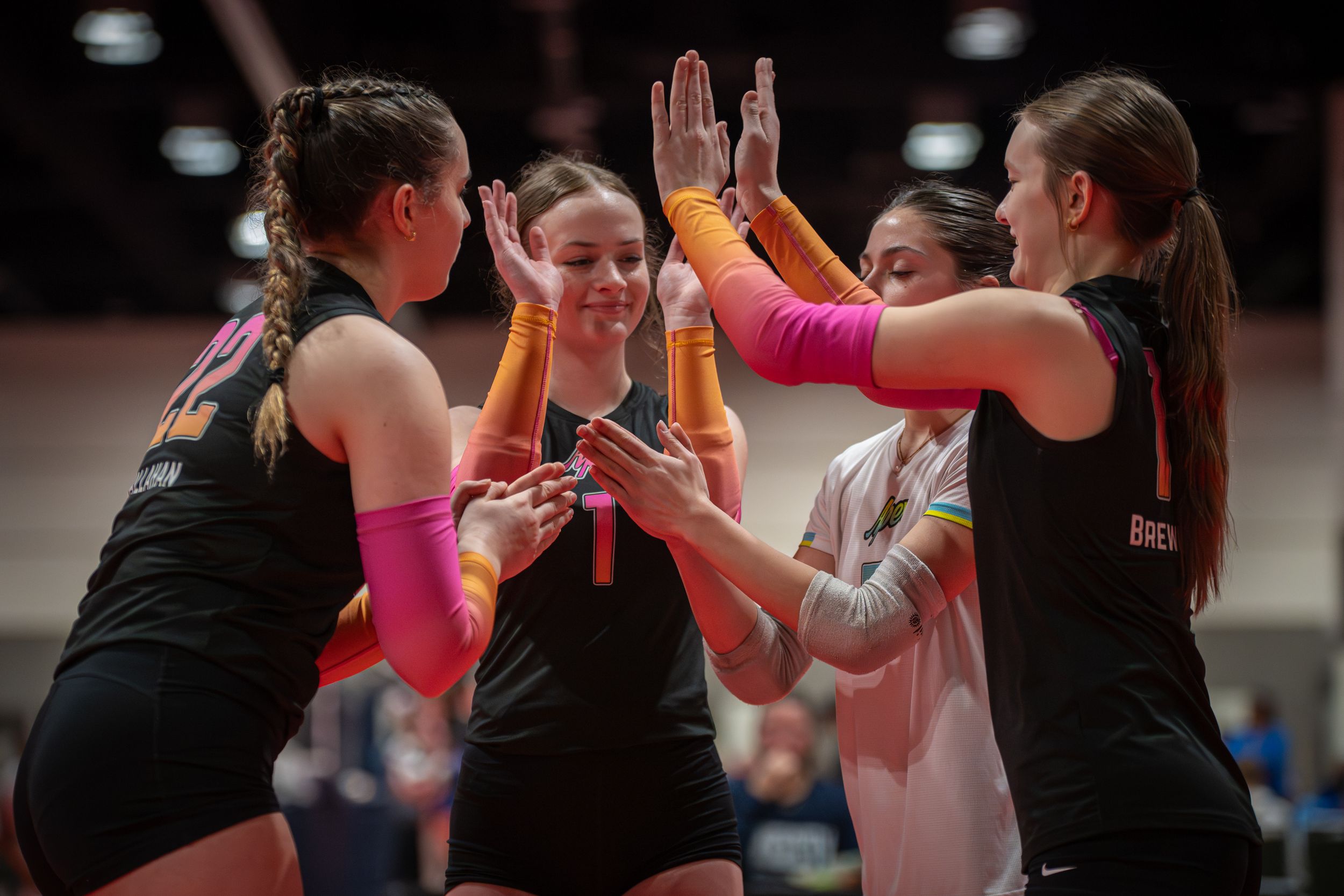 Female volleyball players in black uniforms celebrate with high-fives during a competitive indoor match.