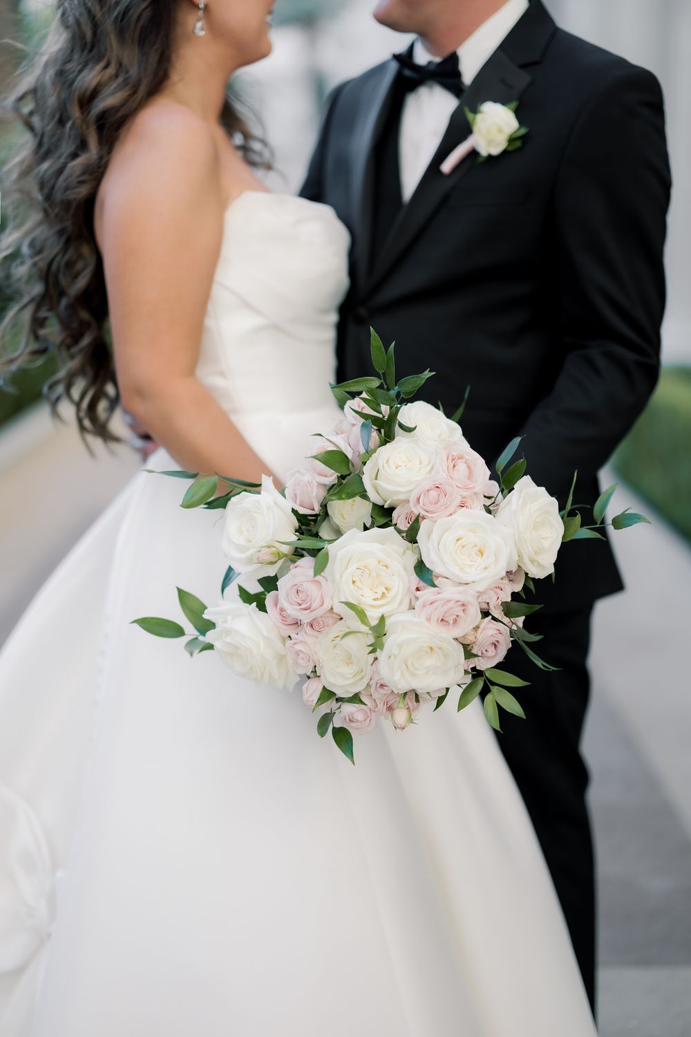 Close-up of bridal bouquet of white and blush pink roses held by couple in wedding attire.