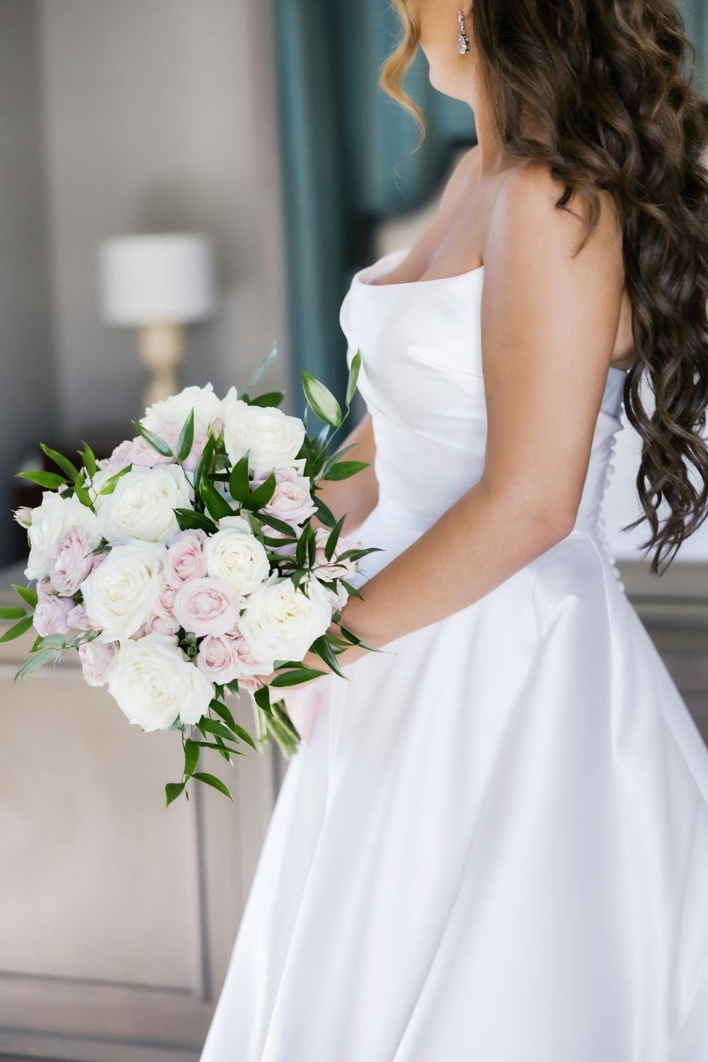 Bride in strapless white satin gown holding elegant bouquet of white and blush pink roses with greenery.