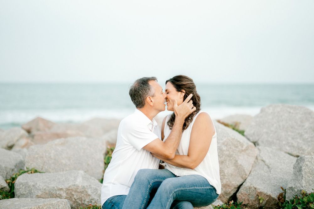 Couple sharing a romantic kiss while sitting on rocks by the ocean on a misty day.
