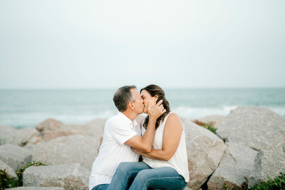 Couple sharing a romantic kiss on rocky shoreline with ocean waves in the background.