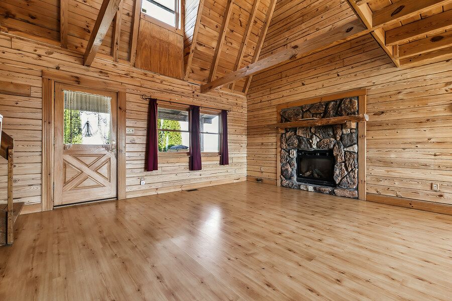 Spacious log cabin living room with vaulted wood ceiling, stone fireplace, and hardwood floors.