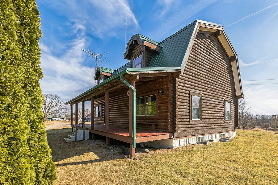 Rustic log cabin exterior with green metal roof, covered porch, and manicured lawn.