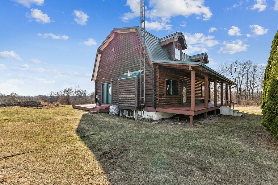 Rustic log cabin home with green metal roof, covered porch, and expansive lawn surrounded by bare trees.